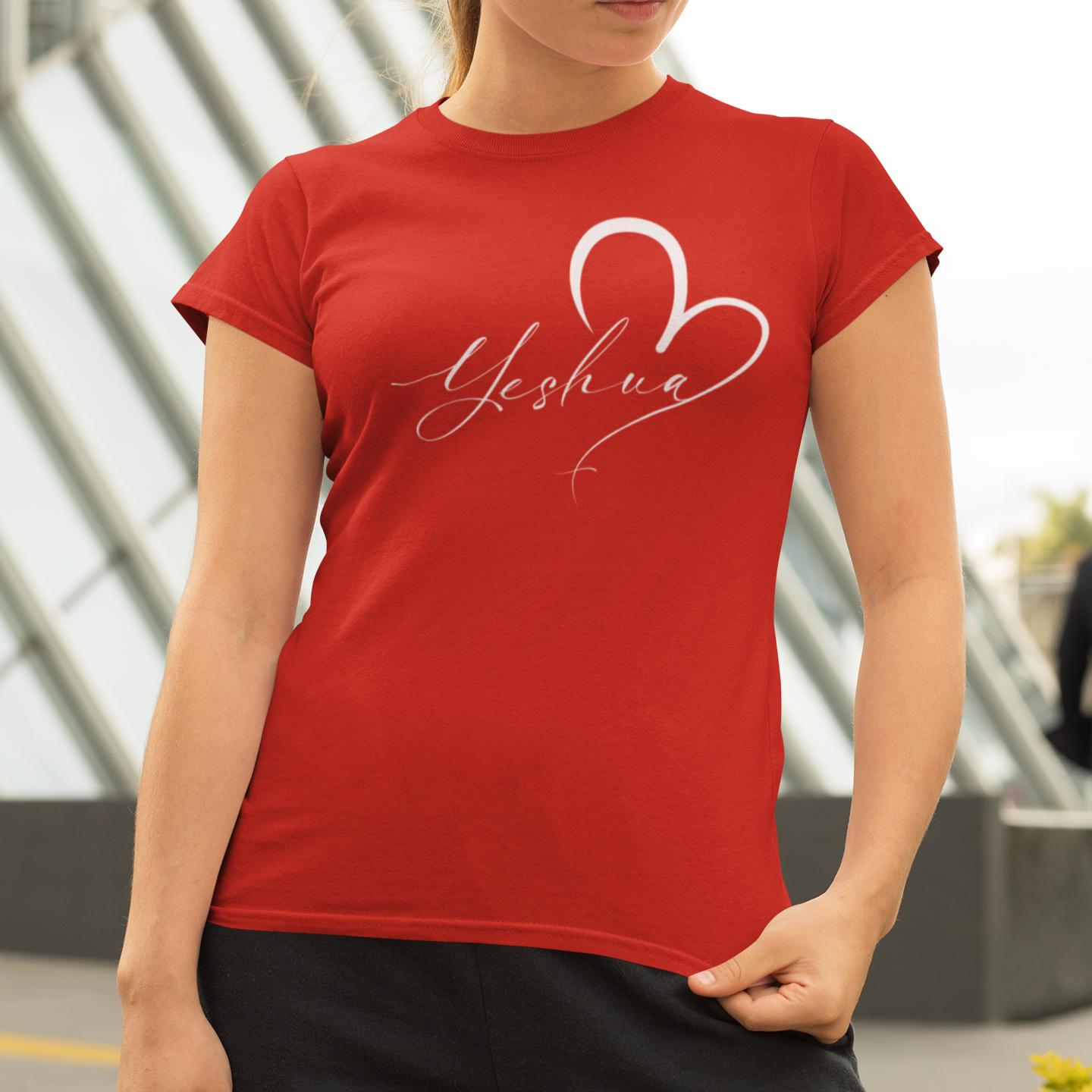 Woman wearing a red t-shirt with 'Yeshua' design outdoors.