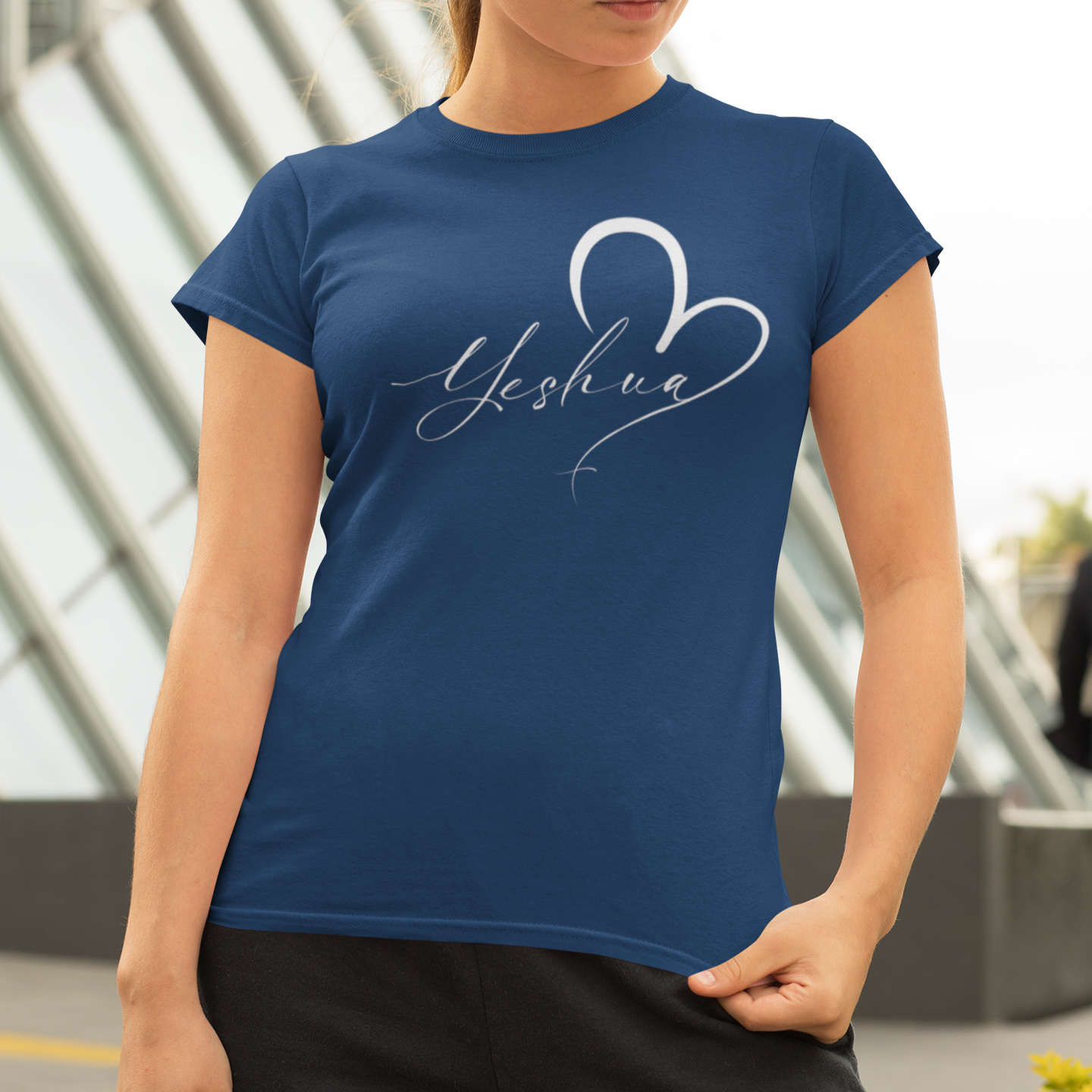 Woman wearing a blue t-shirt with 'Yeshua' design outdoors.