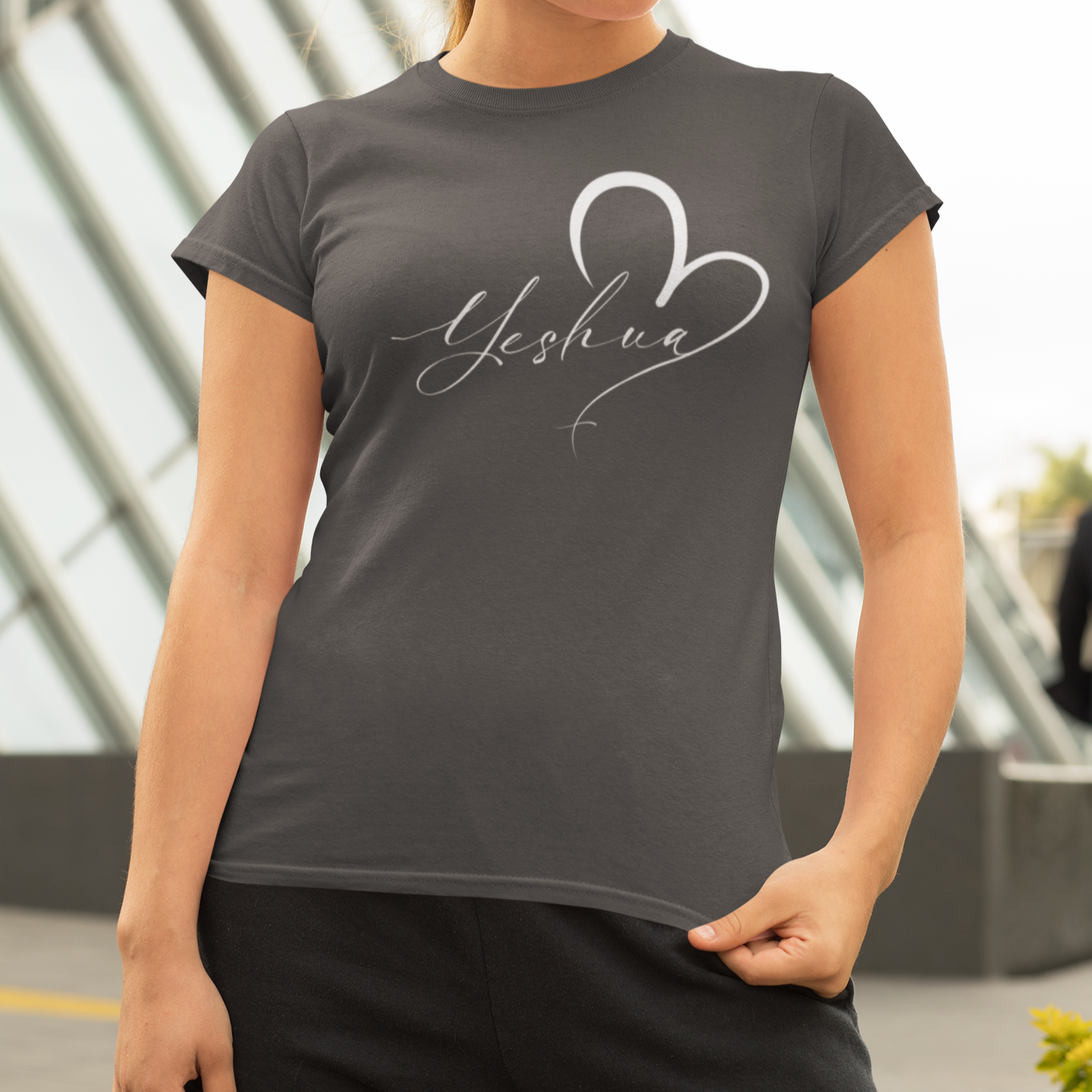 Woman wearing a dark gray t-shirt with 'Yeshua' design outdoors.