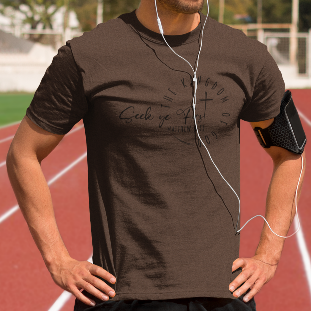 Man standing on a running track wearing a brown t-shirt and earphones.