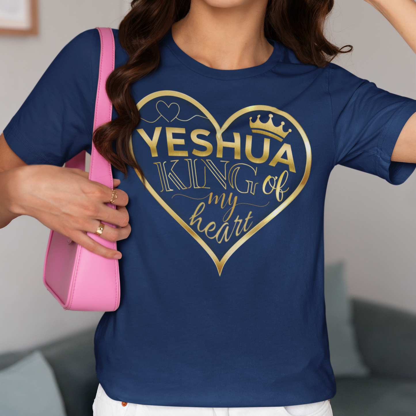 Person wearing a blue t-shirt with 'Yeshua King of my heart' design, holding a pink bag.