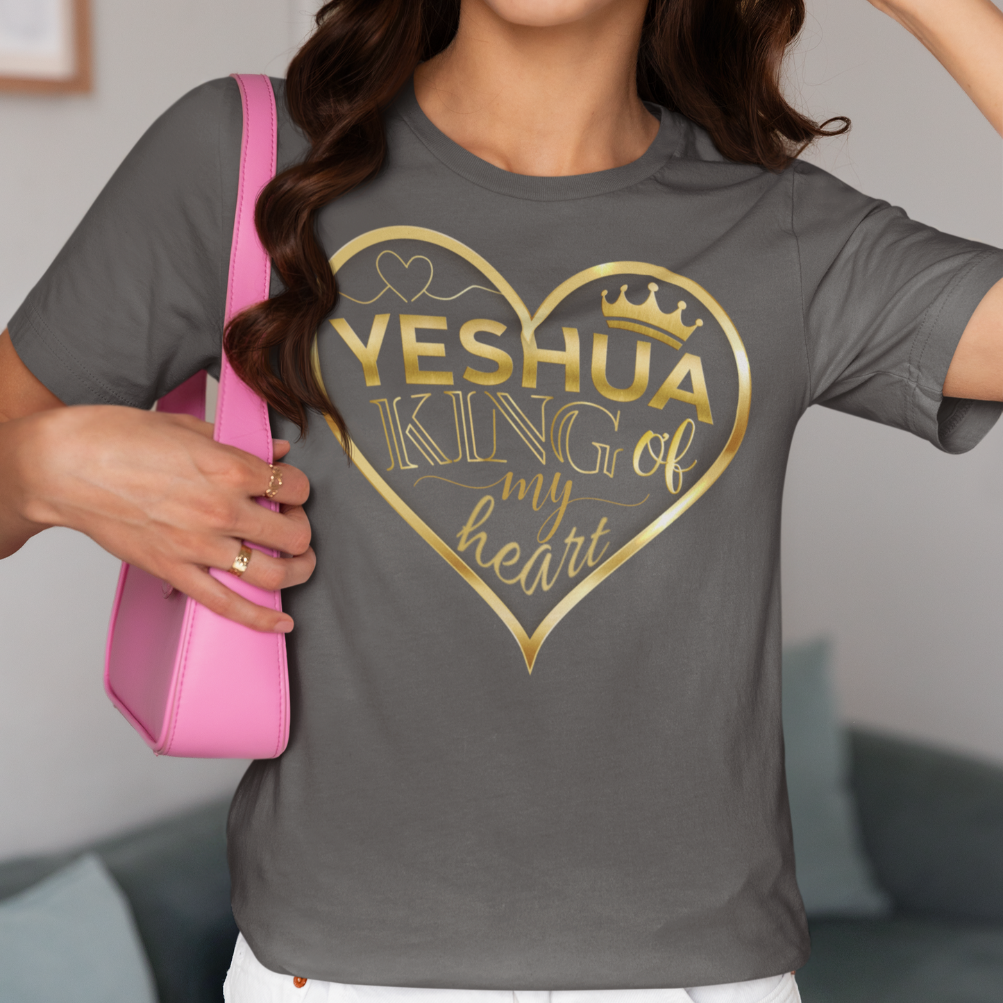 Person wearing a gray t-shirt with 'Yeshua King of my heart' design, holding a pink bag.