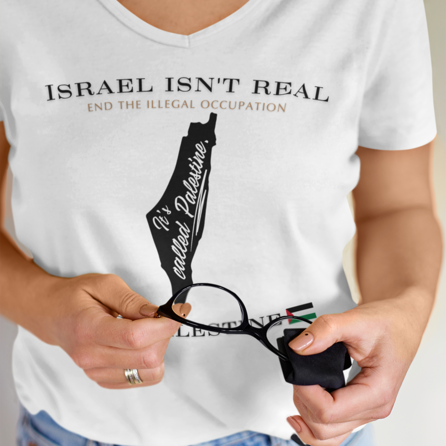 Person wearing a white t-shirt with a graphic and text, holding a pair of glasses.