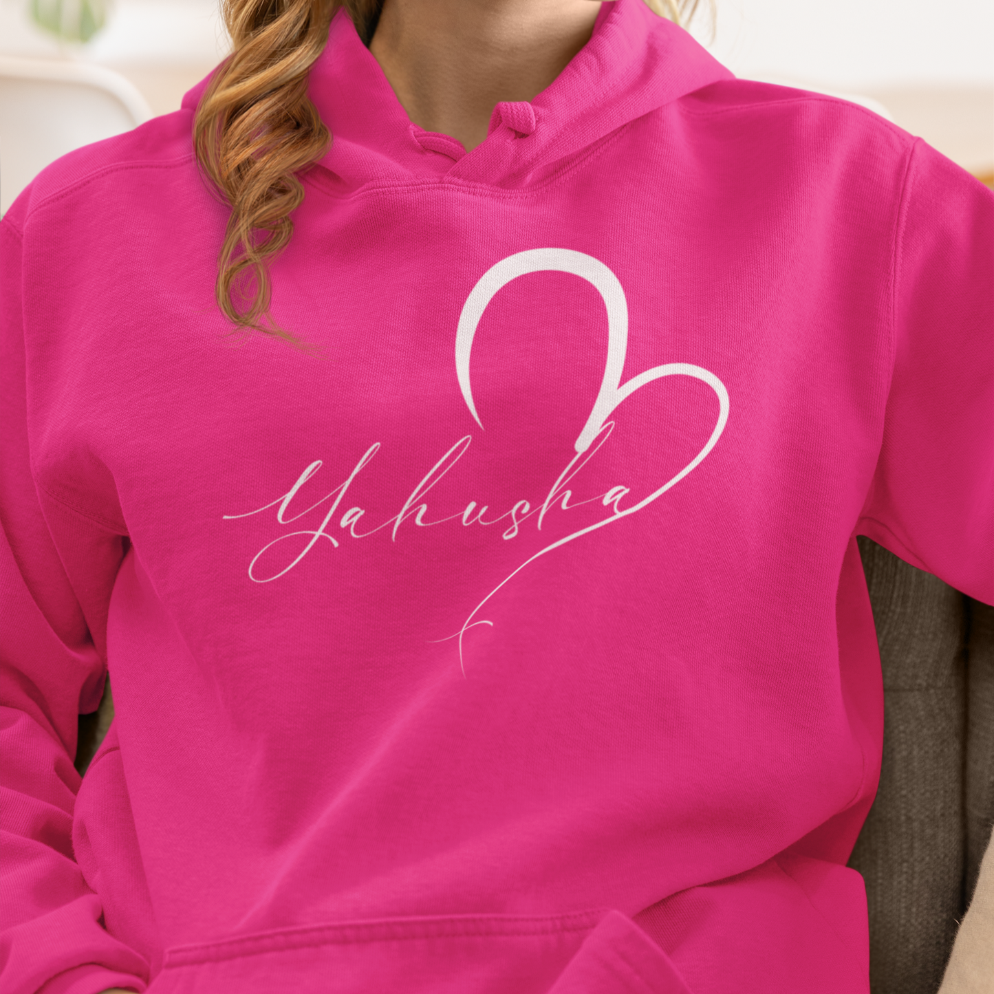 Person wearing a pink hoodie with a heart and text design, sitting on a couch.