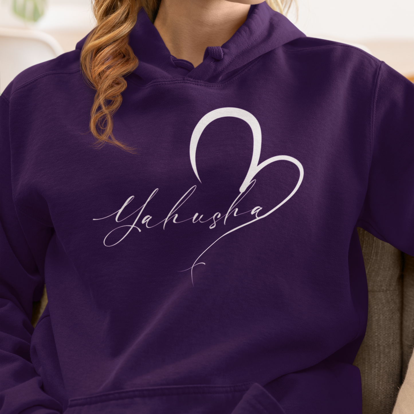 Person wearing a purple hoodie with 'Yahusha' design, sitting on a couch.