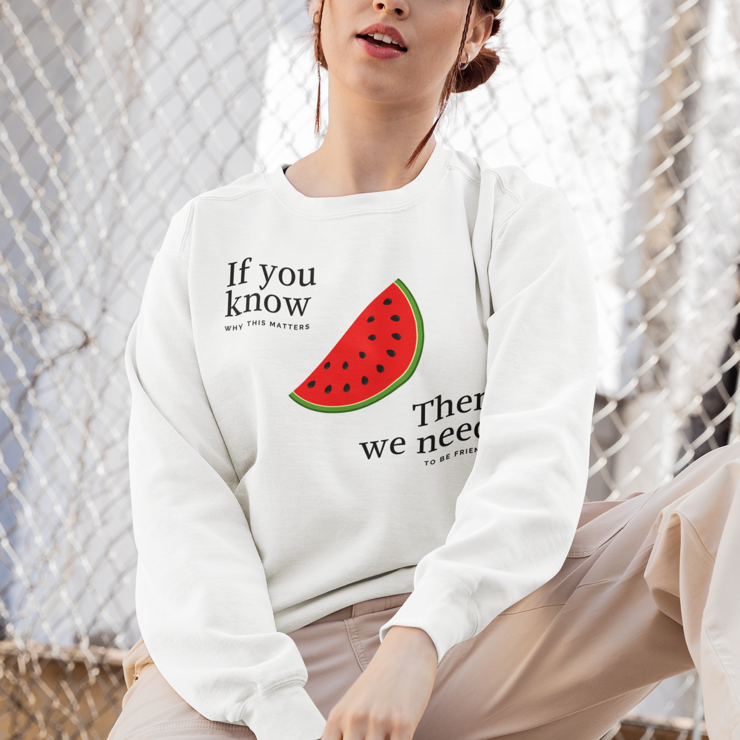 Person wearing a white sweatshirt with a watermelon graphic and text, sitting on a skateboard.