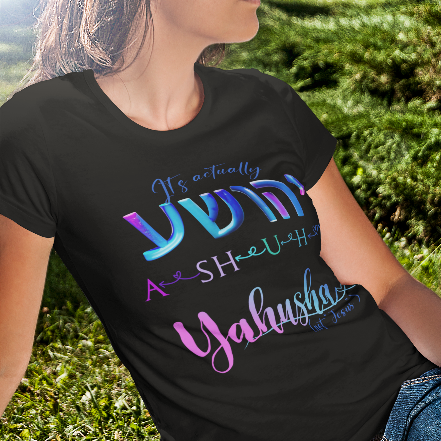 Person wearing a black t-shirt with colorful text design sitting on grass.