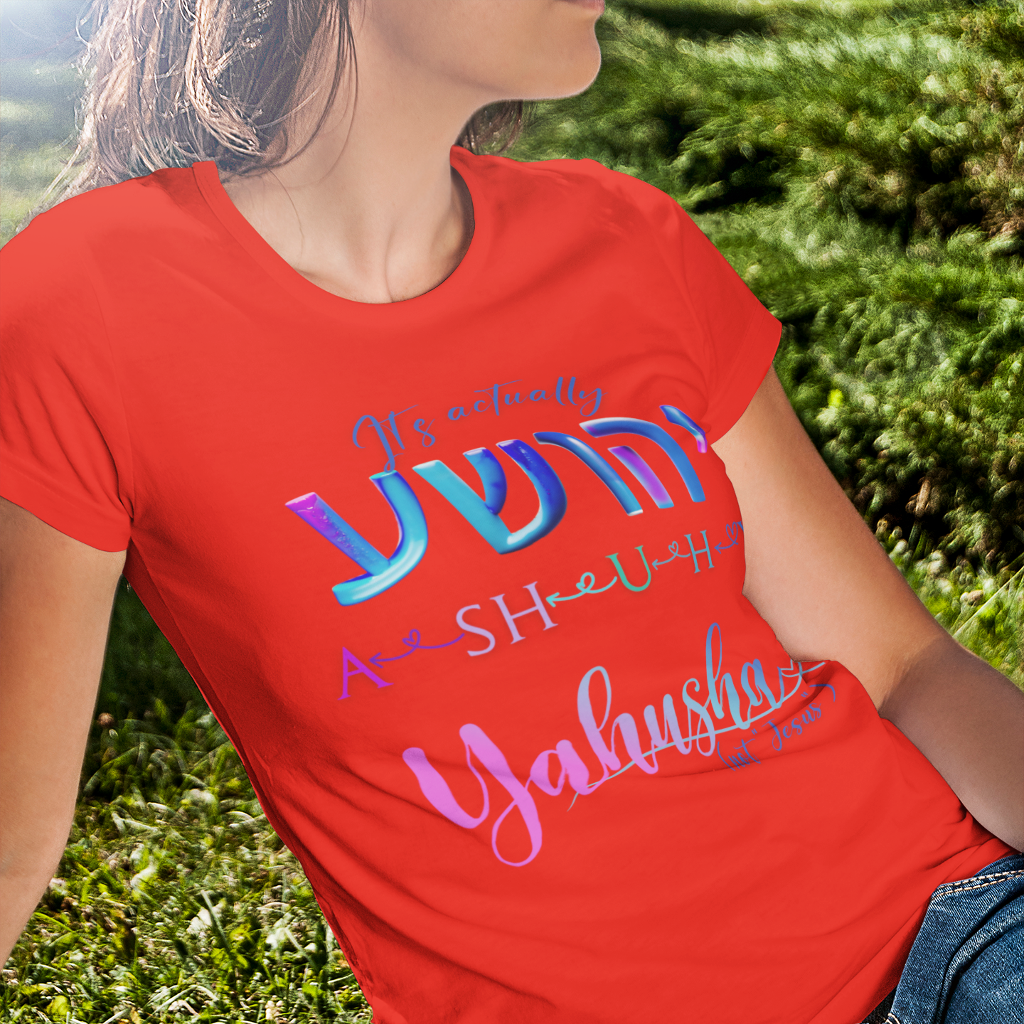 Person wearing a red t-shirt with colorful text sitting on grass