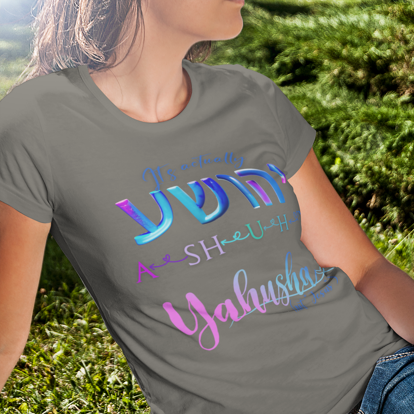 Person wearing a gray t-shirt with colorful text sitting on grass