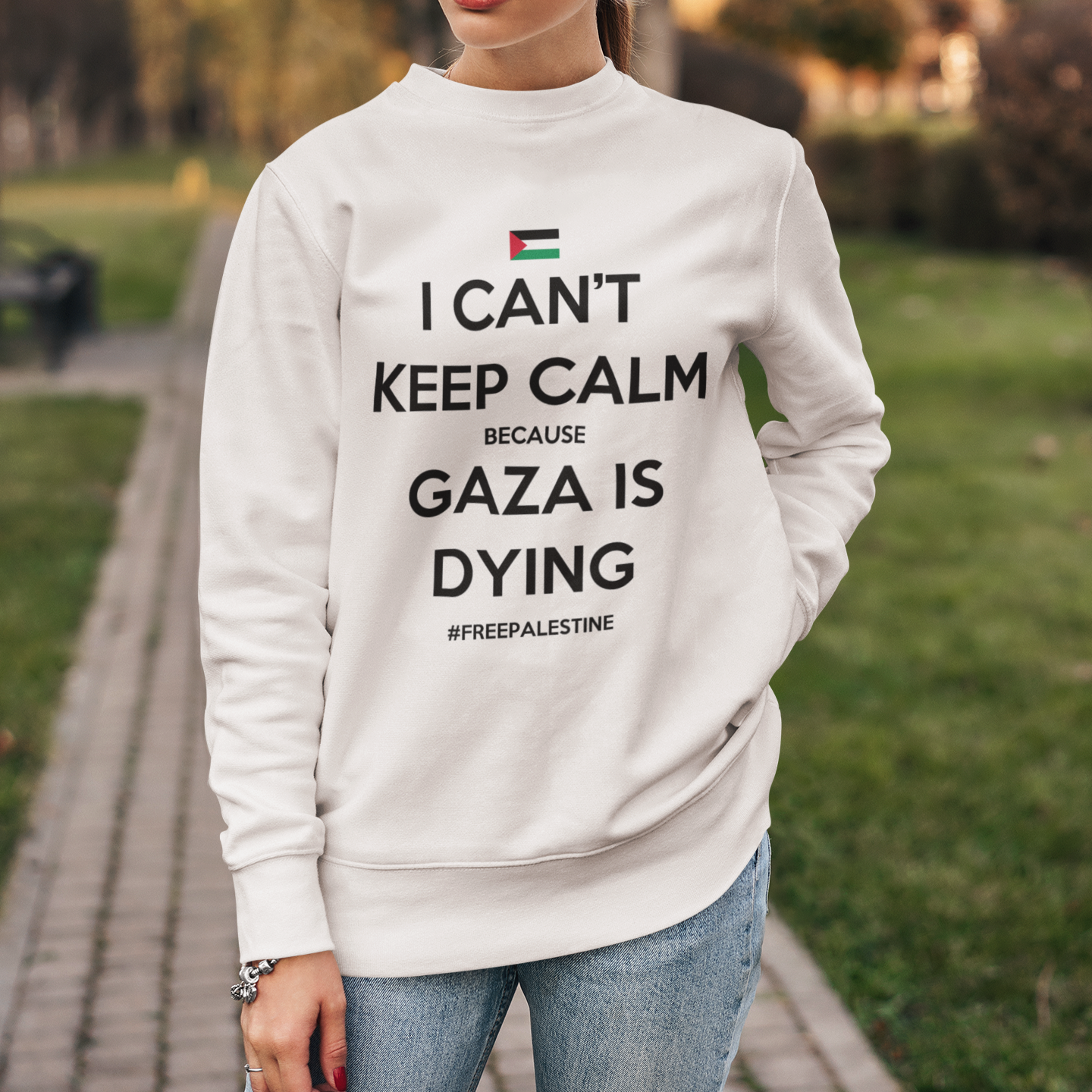 Woman wearing a sweatshirt with a message about Gaza, standing in a park.