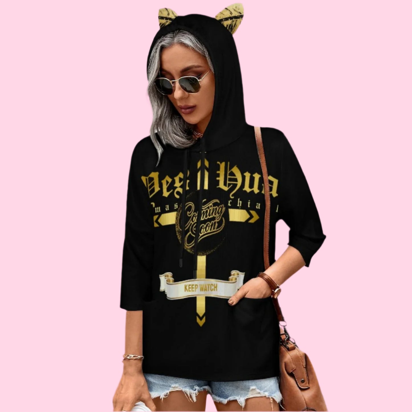 Person wearing a black hoodie with gold text and cat ears on a pink background