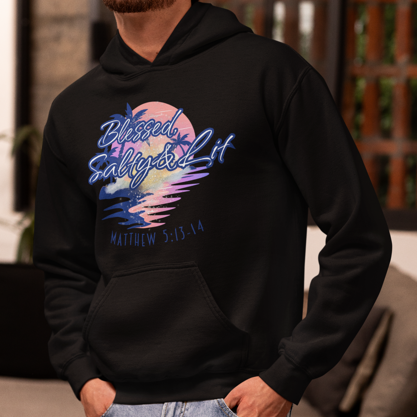 Person wearing a black hoodie with colorful graphic and text, standing indoors.