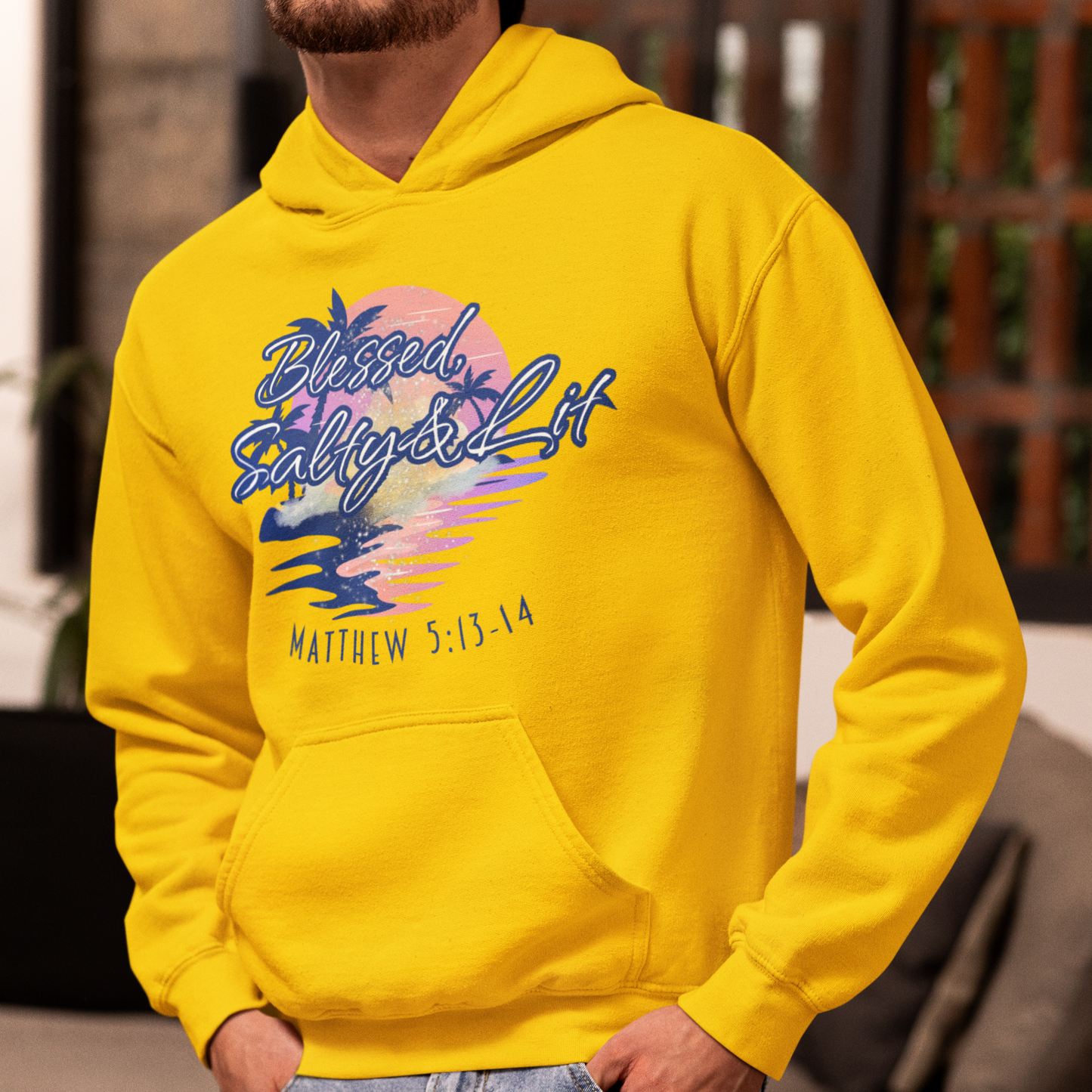 Person wearing a yellow hoodie with a graphic design and text, standing in a room.