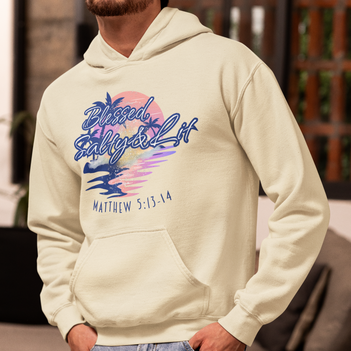 Man wearing a beige hoodie with a colorful graphic and text, standing in a living room.