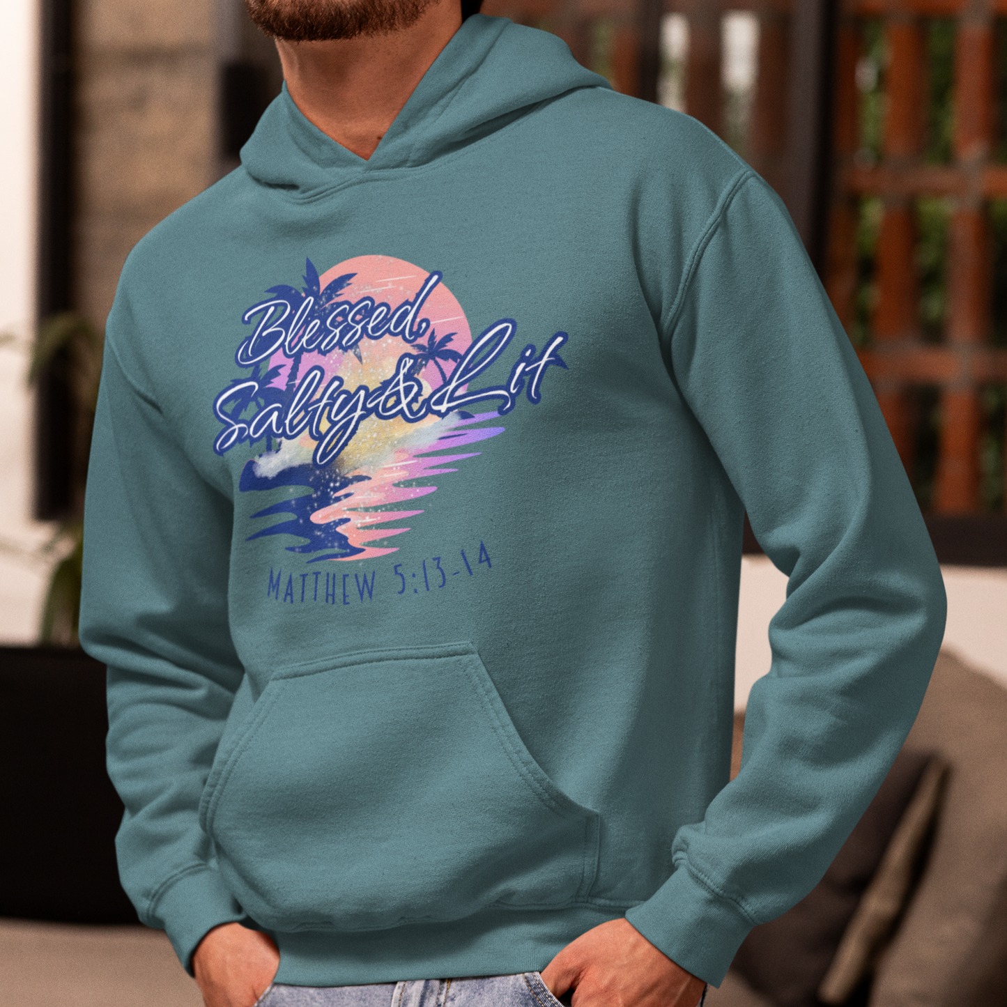 Man wearing a teal hoodie with a colorful graphic design in a living room.