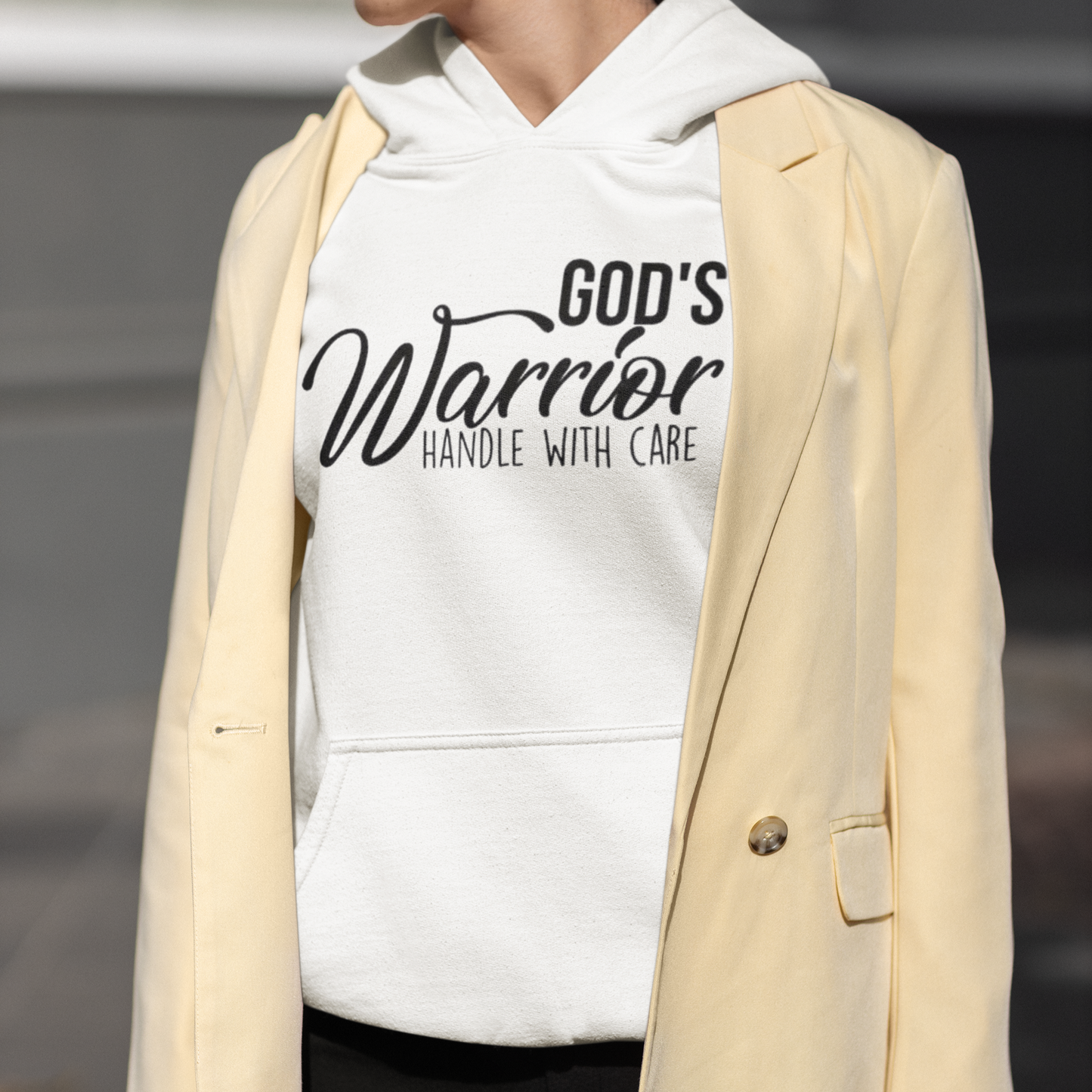 Person wearing a white hoodie with 'God's Warrior Handle with Care' text and a beige blazer.