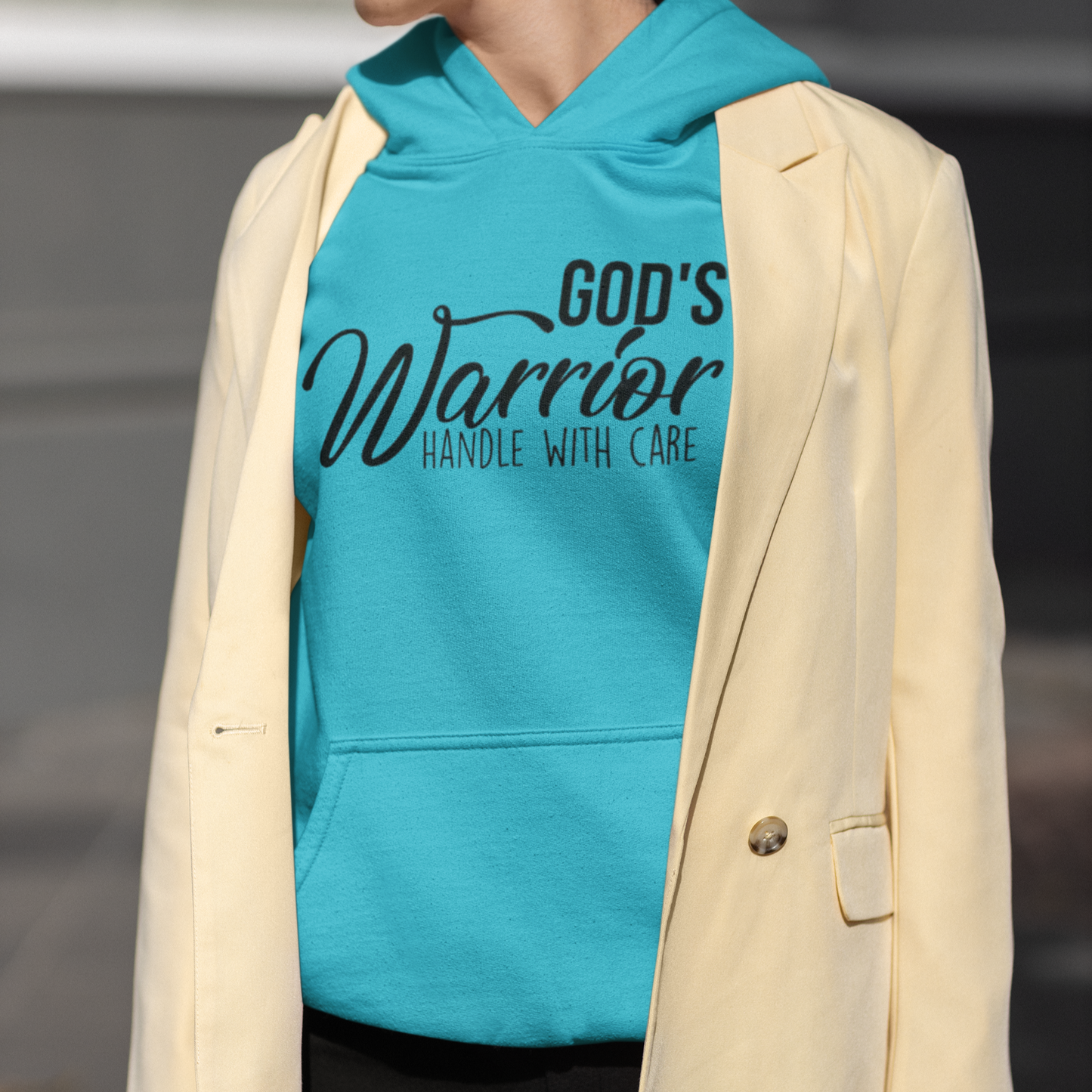 Person wearing a turquoise hoodie with 'God's Warrior Handle with Care' text, paired with a beige blazer.