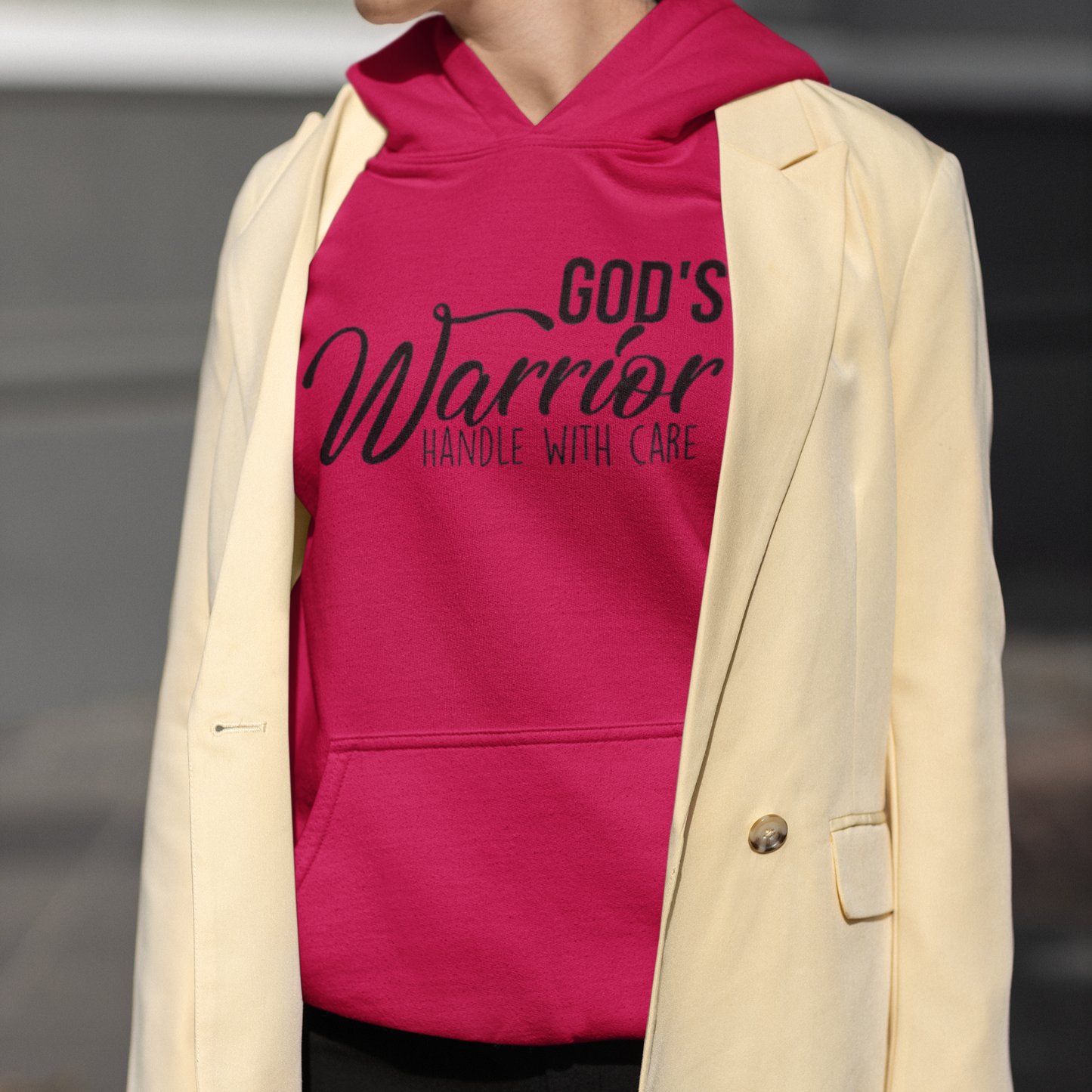 Person wearing a pink hoodie with text and a beige blazer.