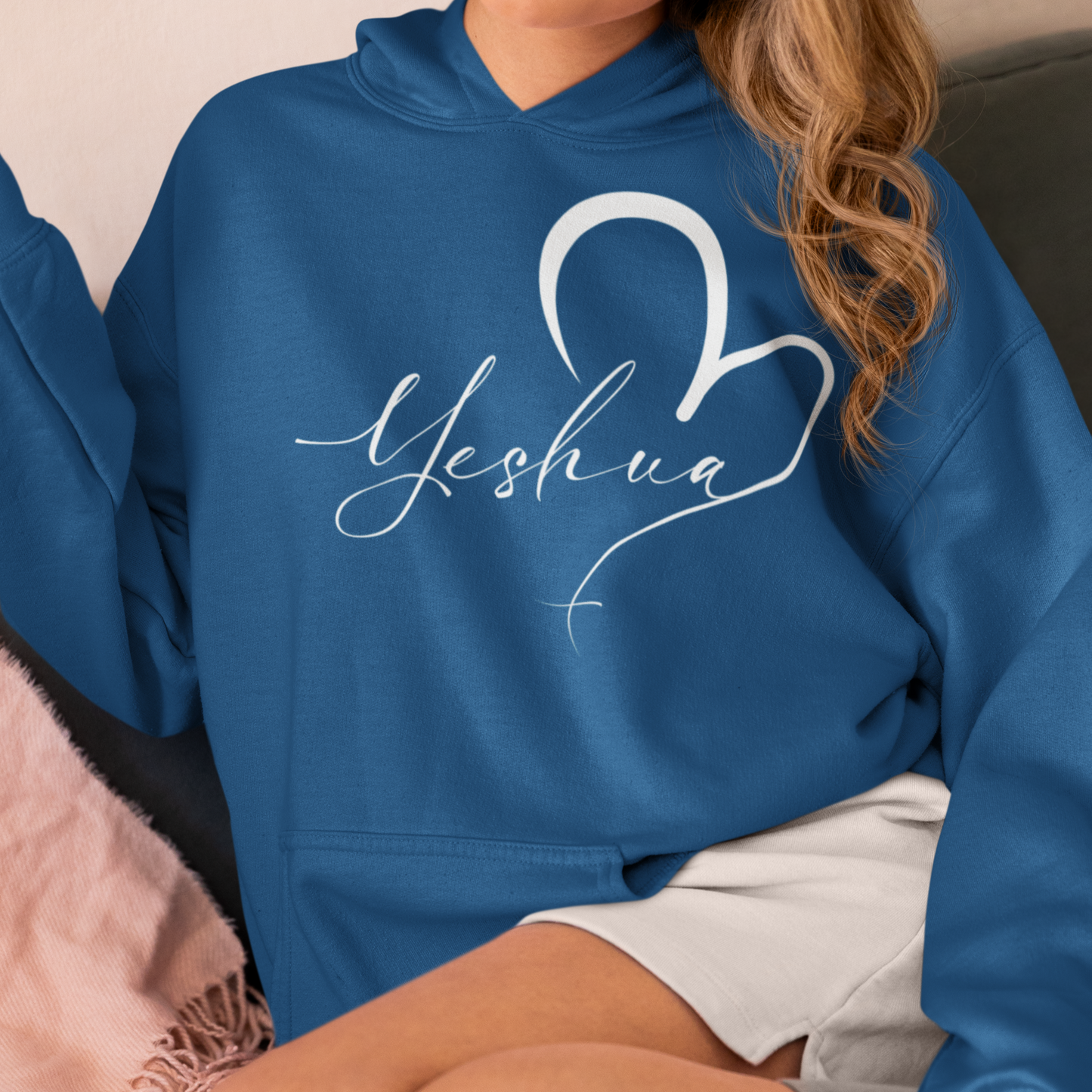 Person wearing a blue hoodie with 'Yeshua' printed on it, sitting on a couch.