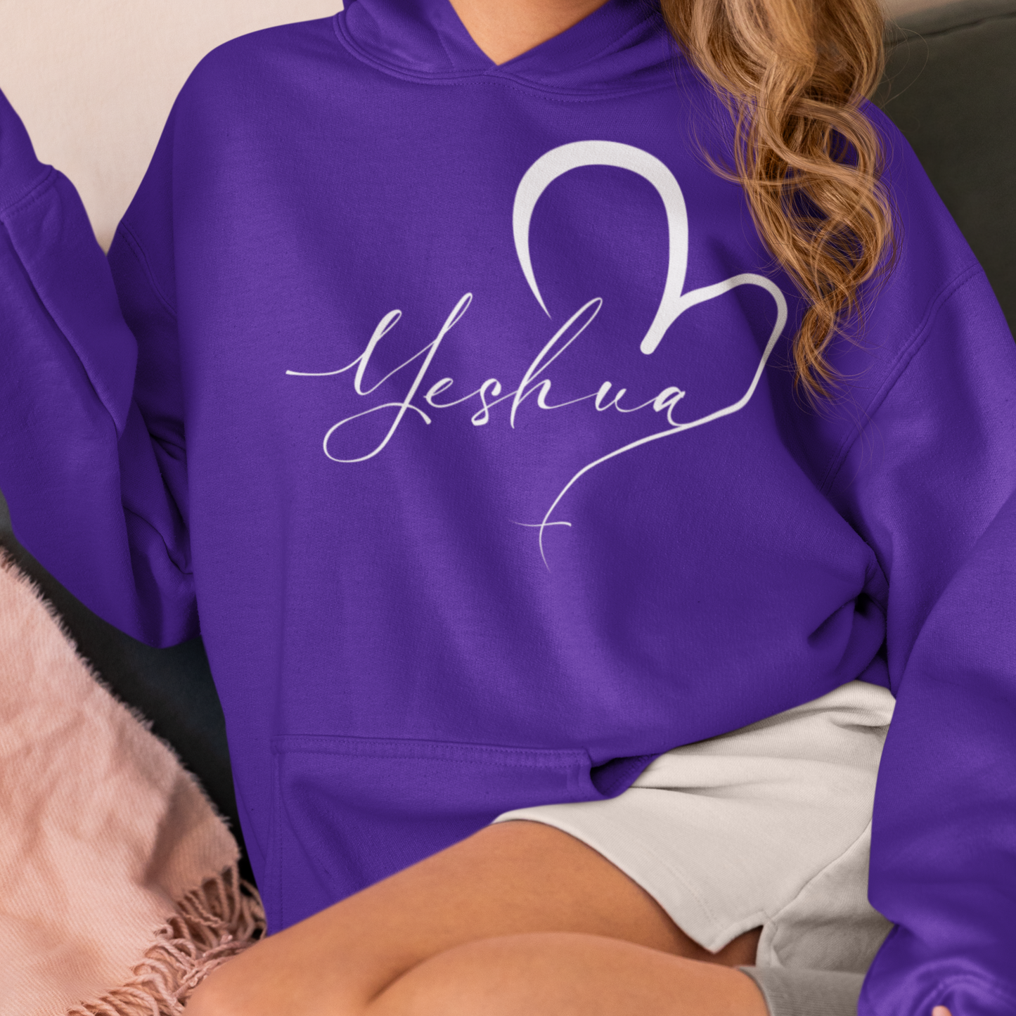 Person wearing a purple hoodie with 'Yeshua' and a heart design.