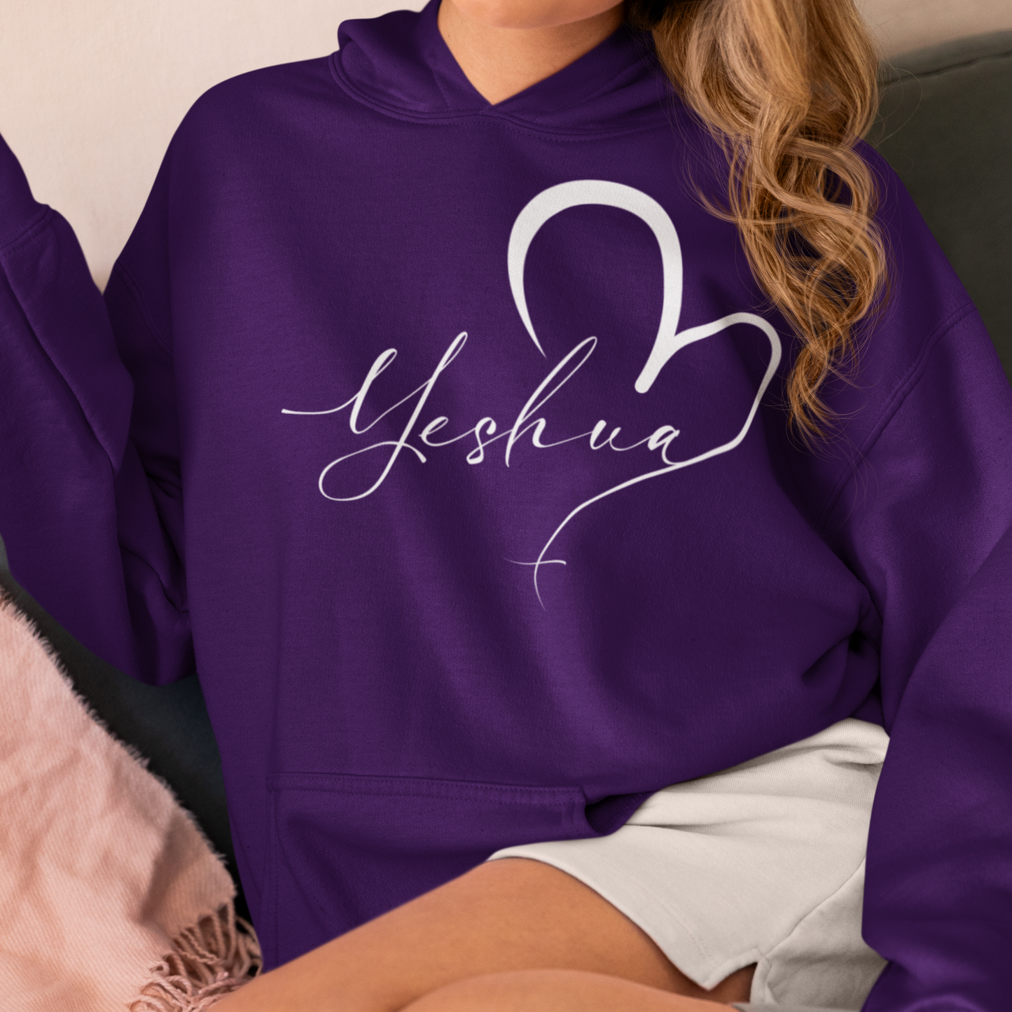 Person wearing a purple hoodie with 'Yeshua' design sitting on a couch.