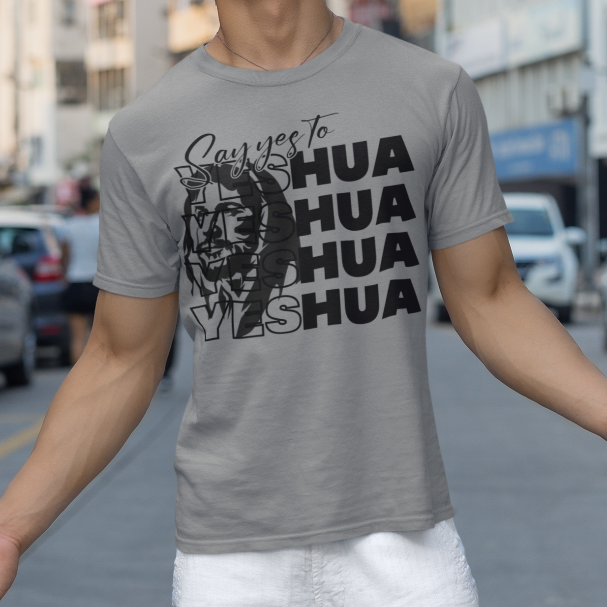 Man wearing a gray t-shirt with 'HUA' text on a city street