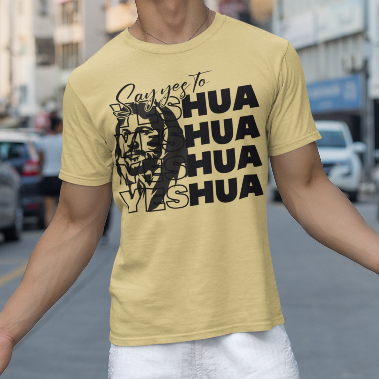 Person wearing a yellow t-shirt with text and graphics on a city street.