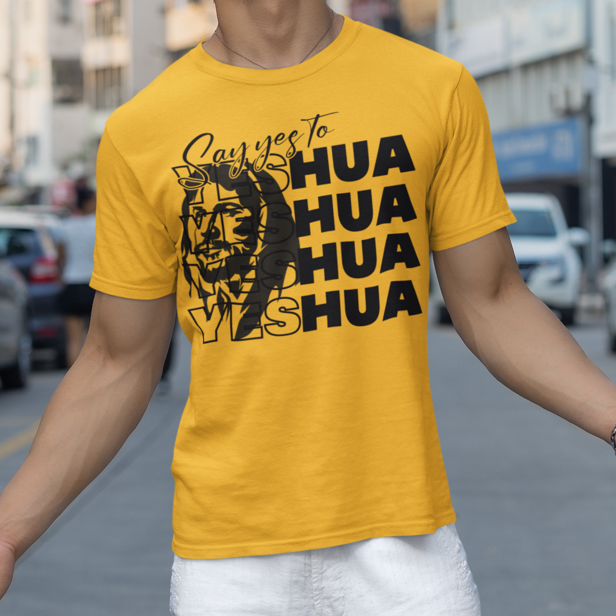 Person wearing a yellow t-shirt with text and graphics on a city street.