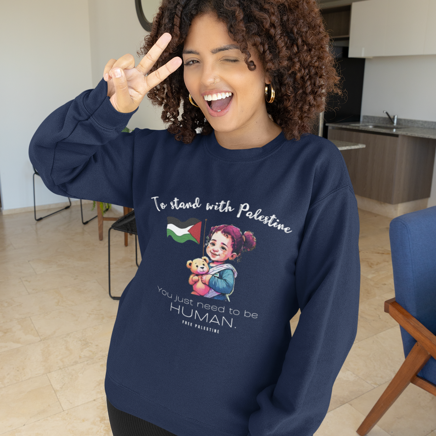 Woman wearing a navy blue sweatshirt with a graphic design and text, standing in a modern indoor setting.
