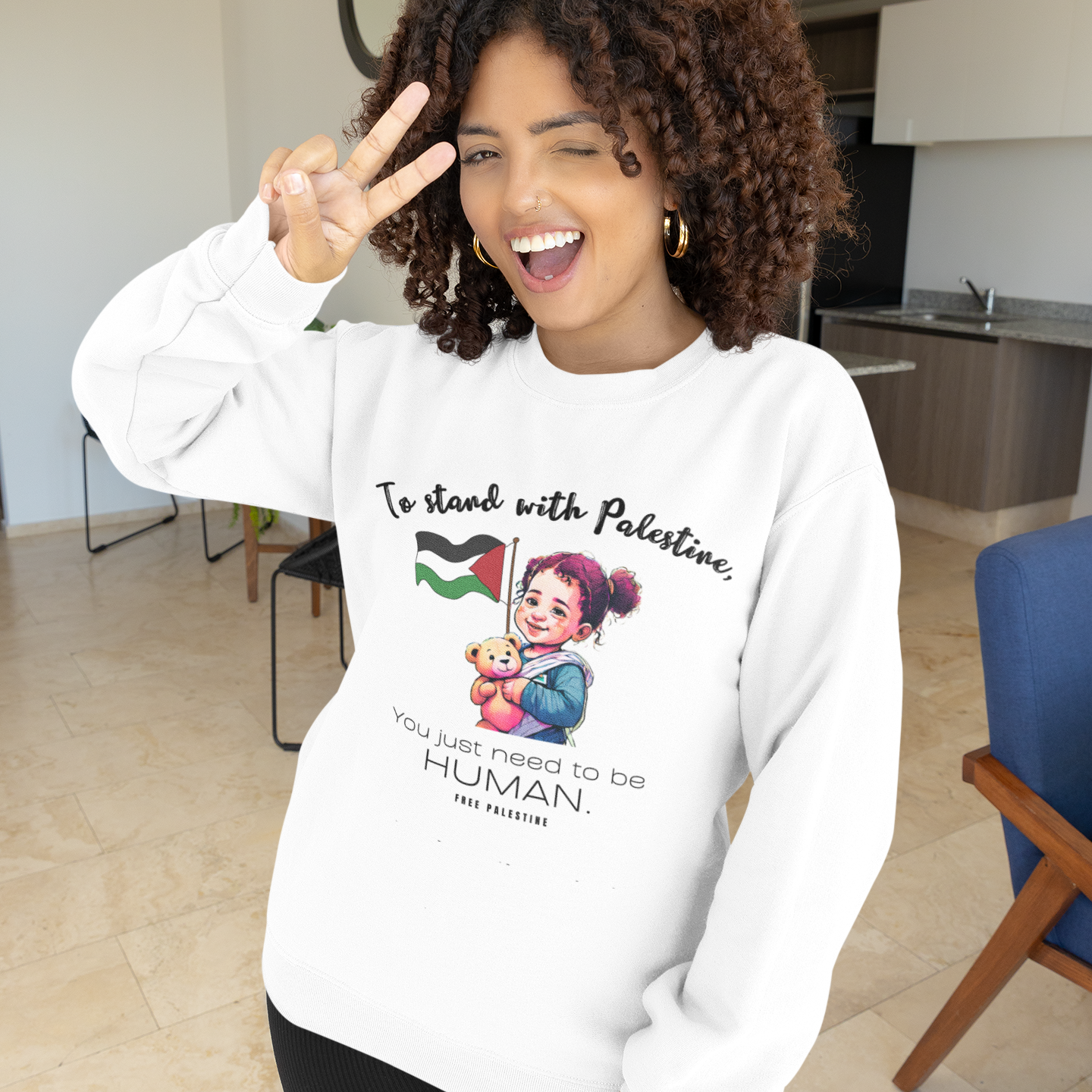 Person wearing a white sweatshirt with a graphic and text, standing in a modern indoor setting.