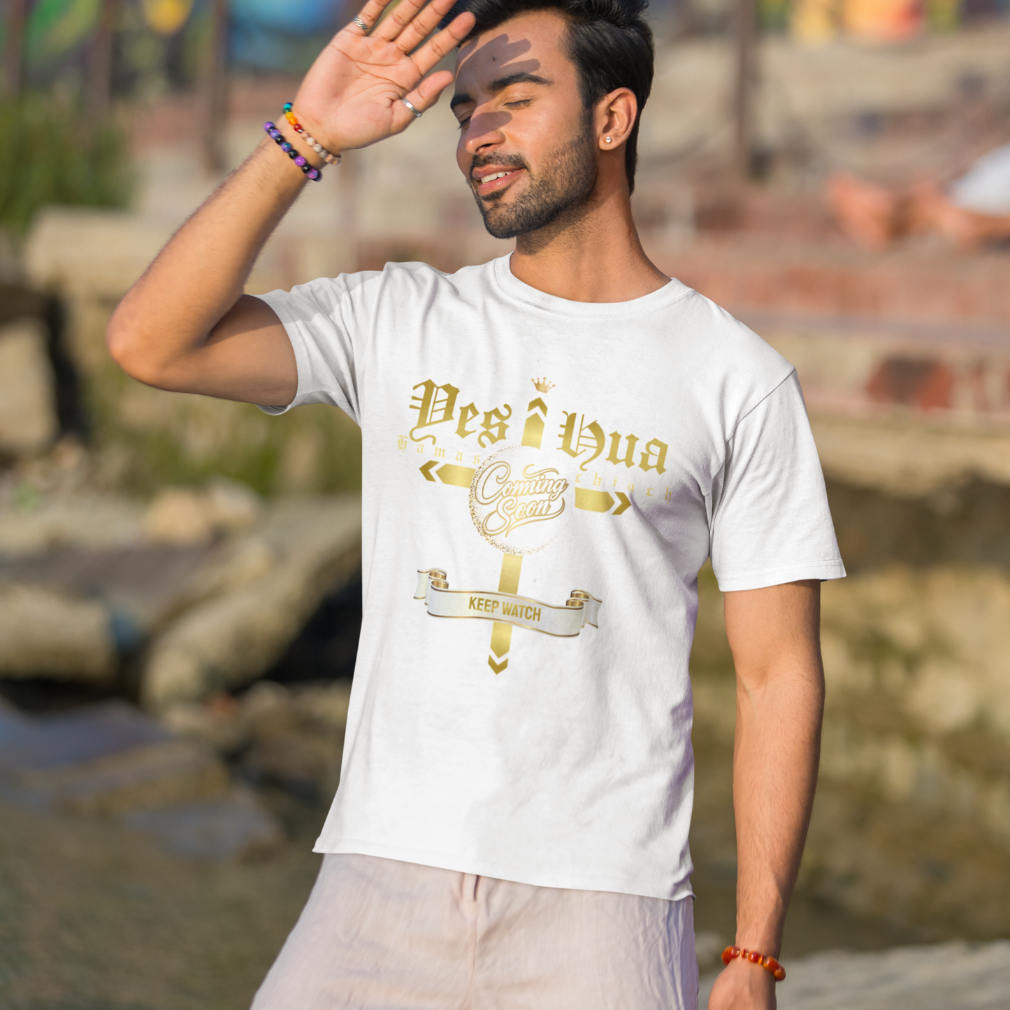 Man wearing a white t-shirt with gold text and design, standing outdoors with a colorful mural in the background.