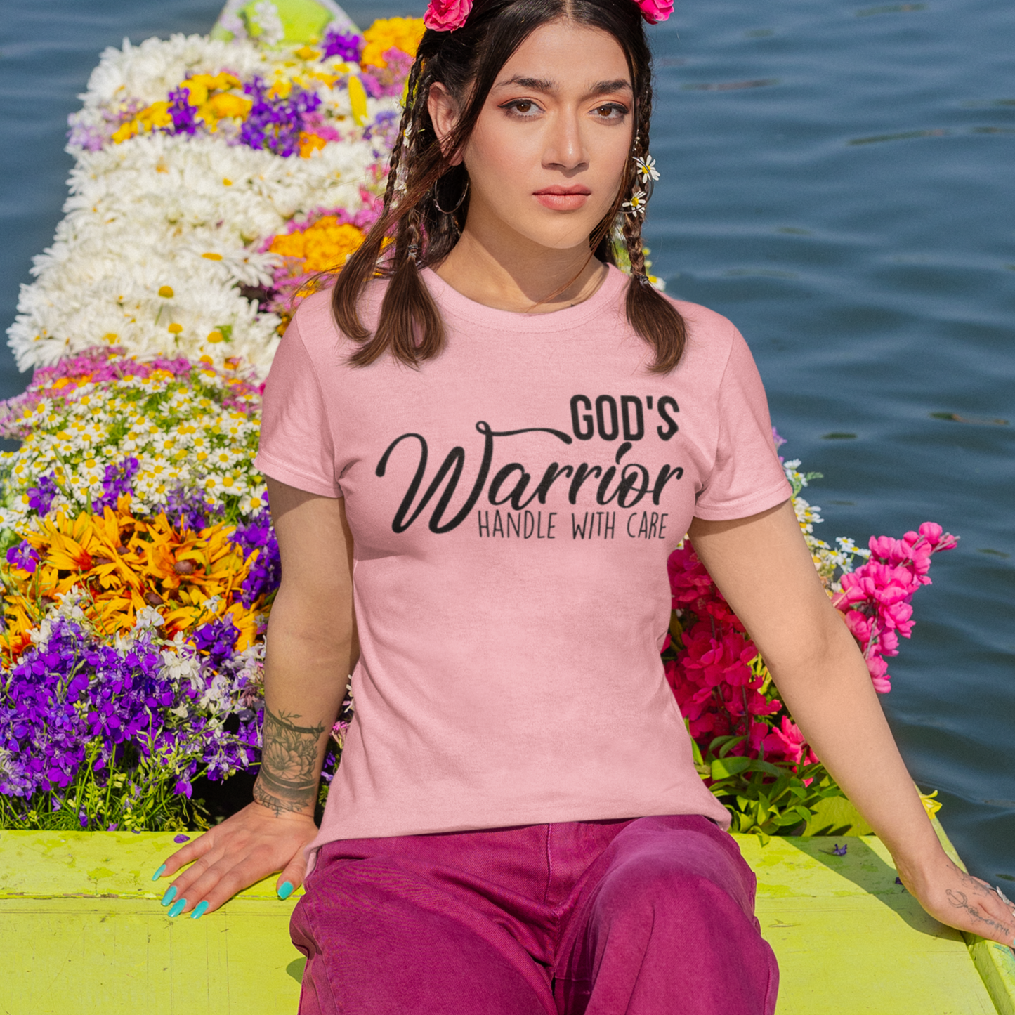 Person wearing a pink t-shirt with 'God's Warrior Handle with Care' text, sitting in a colorful boat on water.