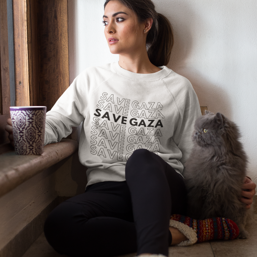 Woman sitting by a window wearing a 'Save Gaza' sweater with a cat on her lap.
