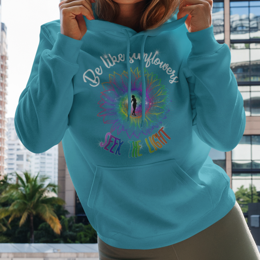 Woman wearing a turquoise hoodie with colorful text and design, standing in front of city buildings.