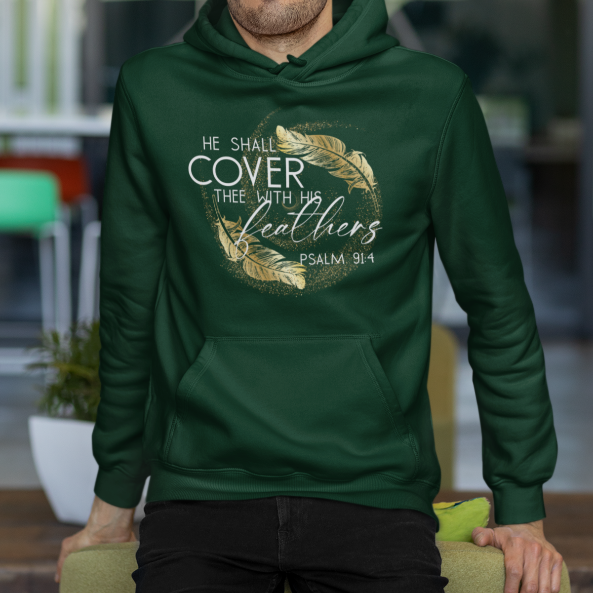 Man wearing a green hoodie with text and design, sitting on a chair indoors.