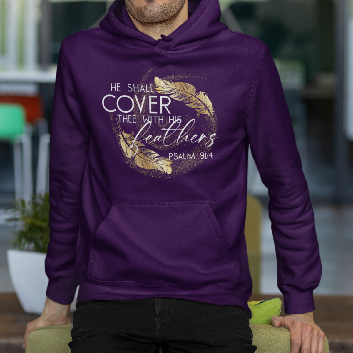 Man wearing a purple hoodie with text and feather design, standing in an outdoor setting.