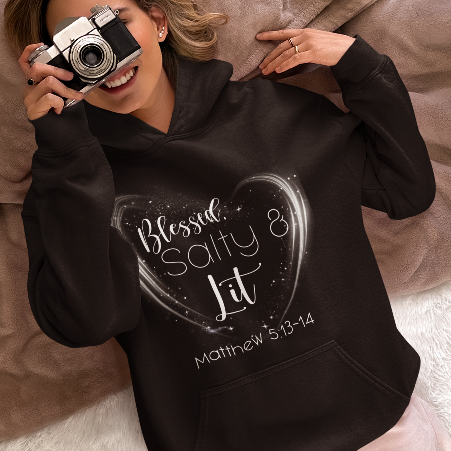 Person wearing a black hoodie with text, holding a camera.