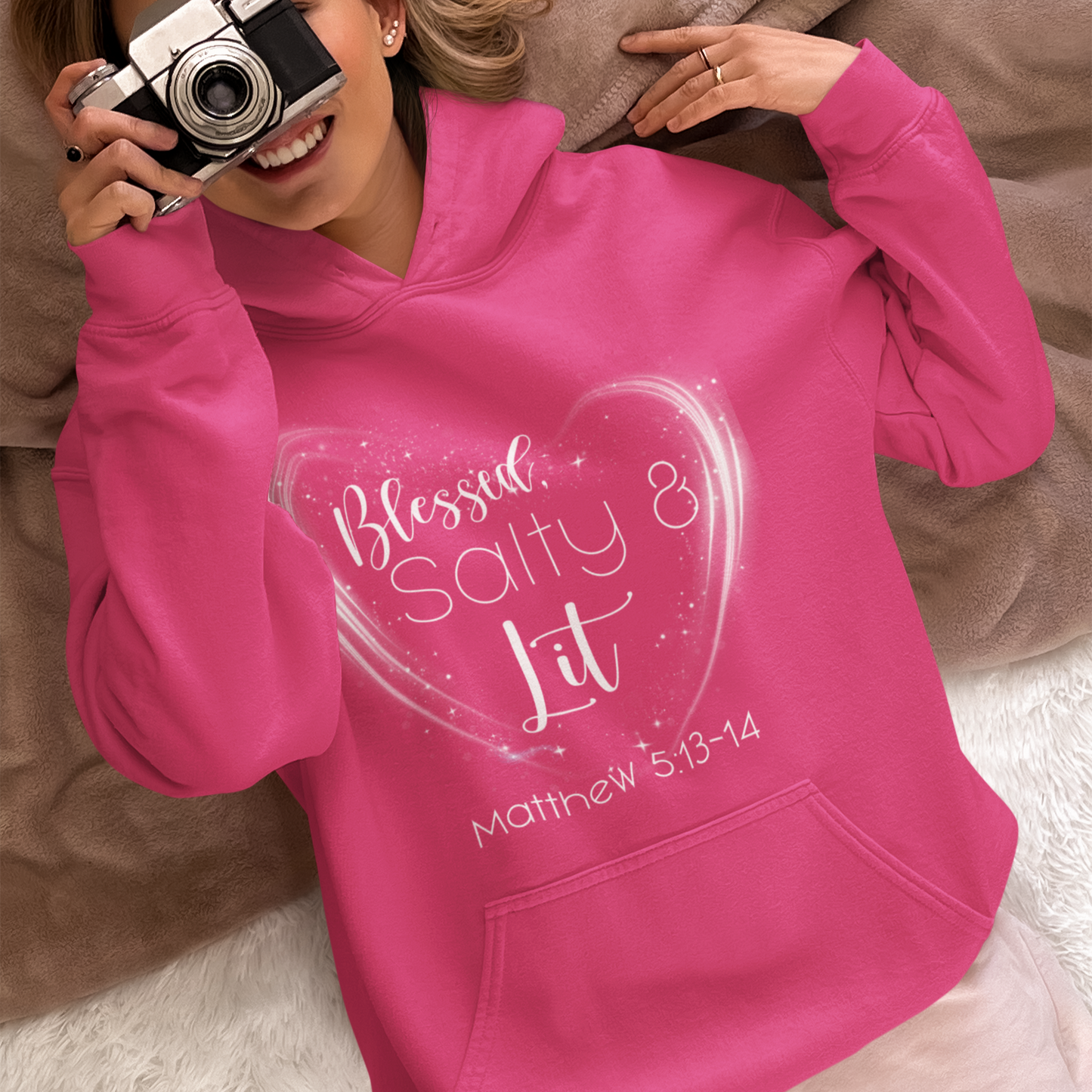 Person wearing a pink hoodie with text, holding a camera on a beige couch.
