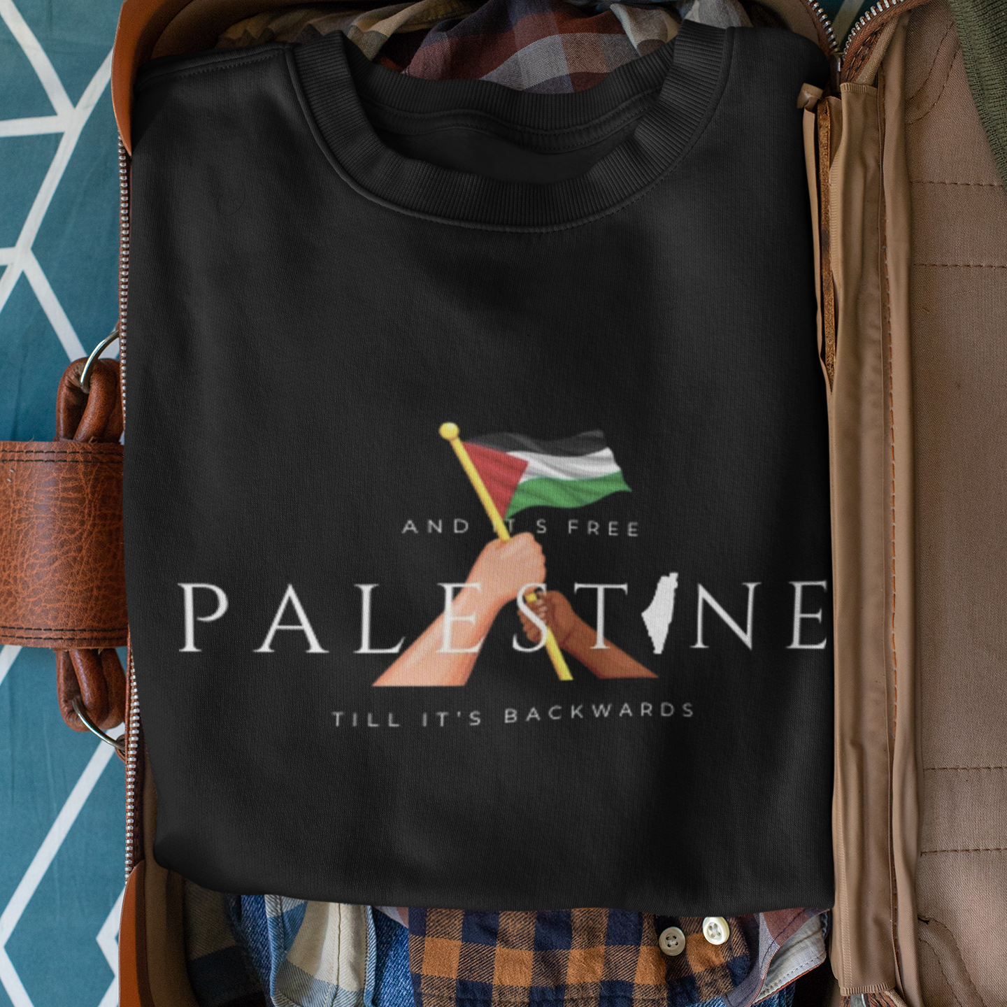 Black t-shirt with a design and text on a suitcase with clothes inside, against a blue geometric patterned background.
