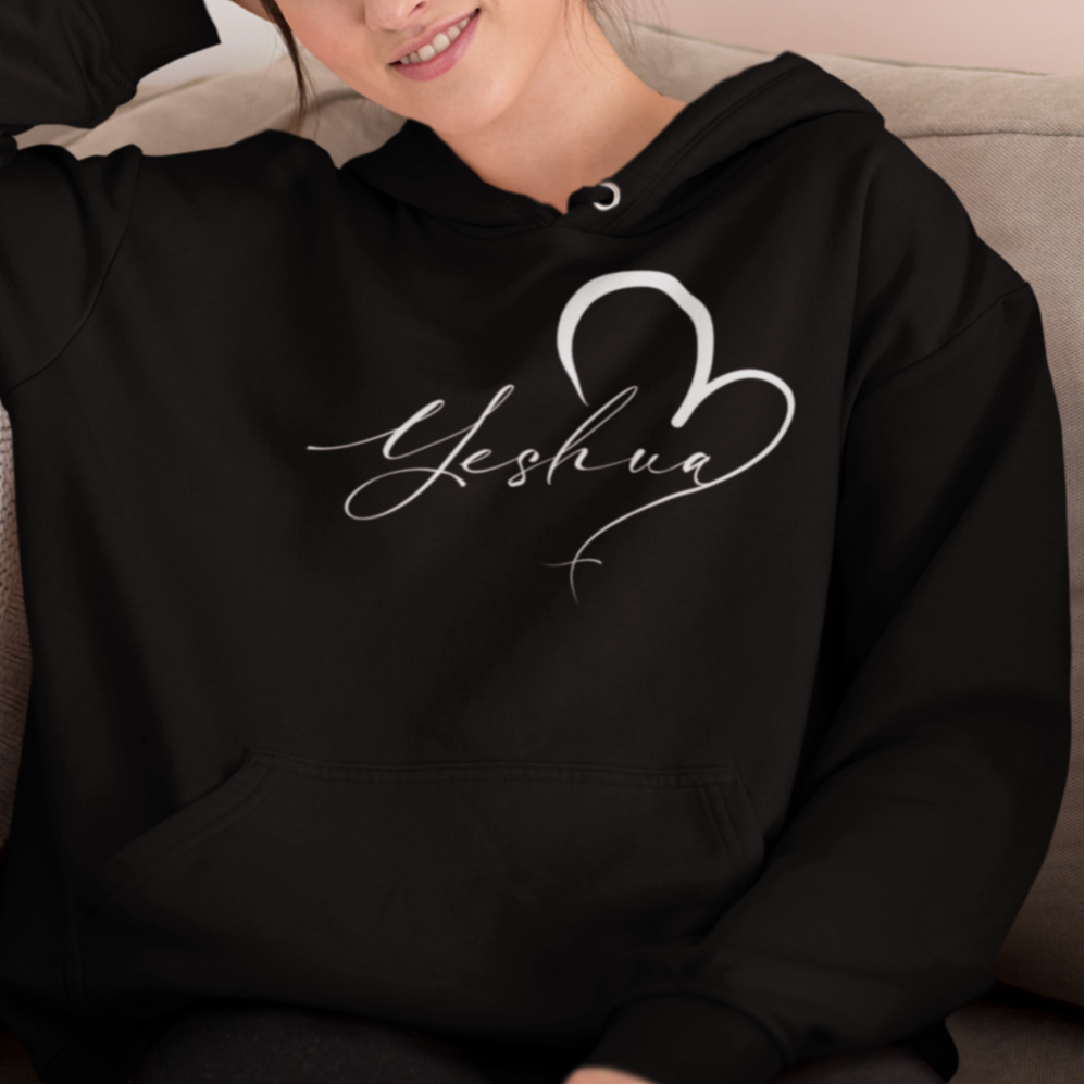 Woman wearing a black hoodie with 'Yeshua' design sitting on a couch.