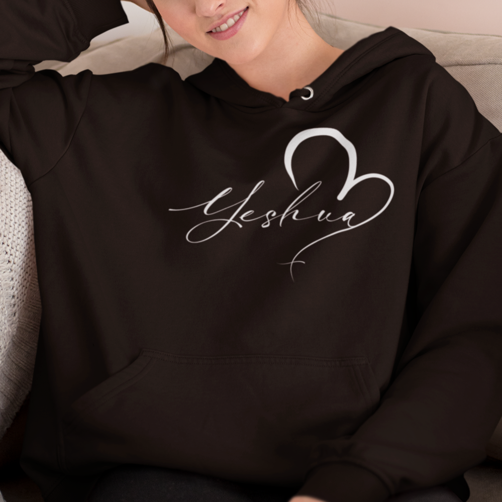 Woman wearing a black hoodie with 'Yeshua' design, sitting on a couch.