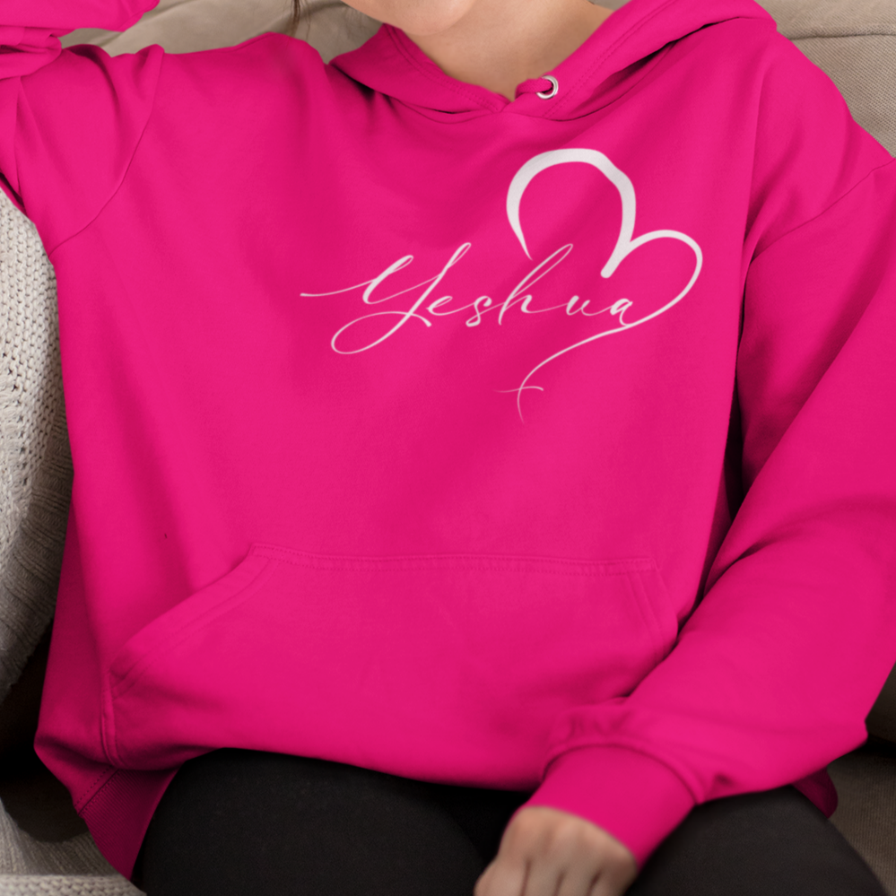 Woman wearing a bright pink hoodie with 'Yeshiva' design, sitting on a couch.