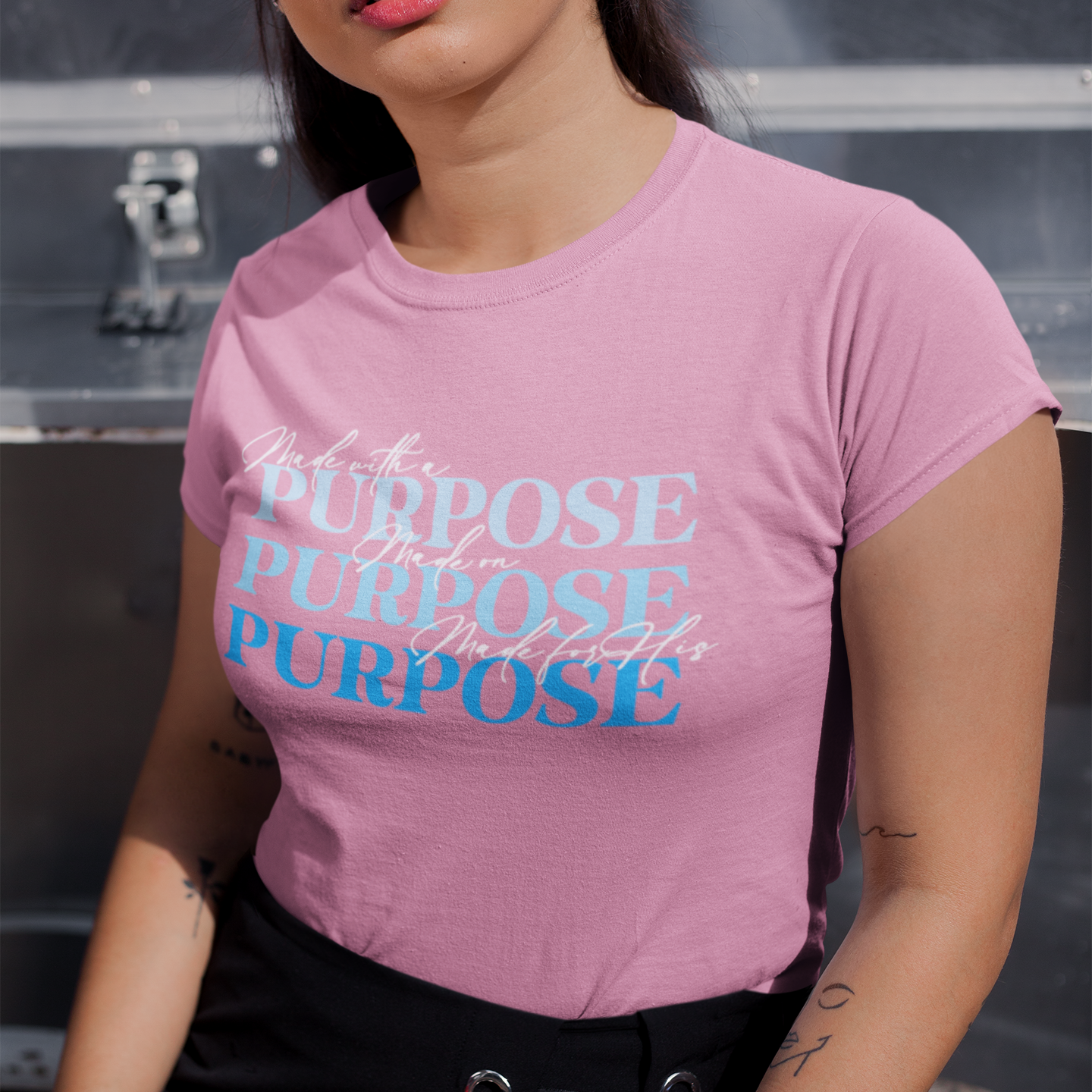 Woman wearing a pink t-shirt with 'purpose' text, standing against a dark background.