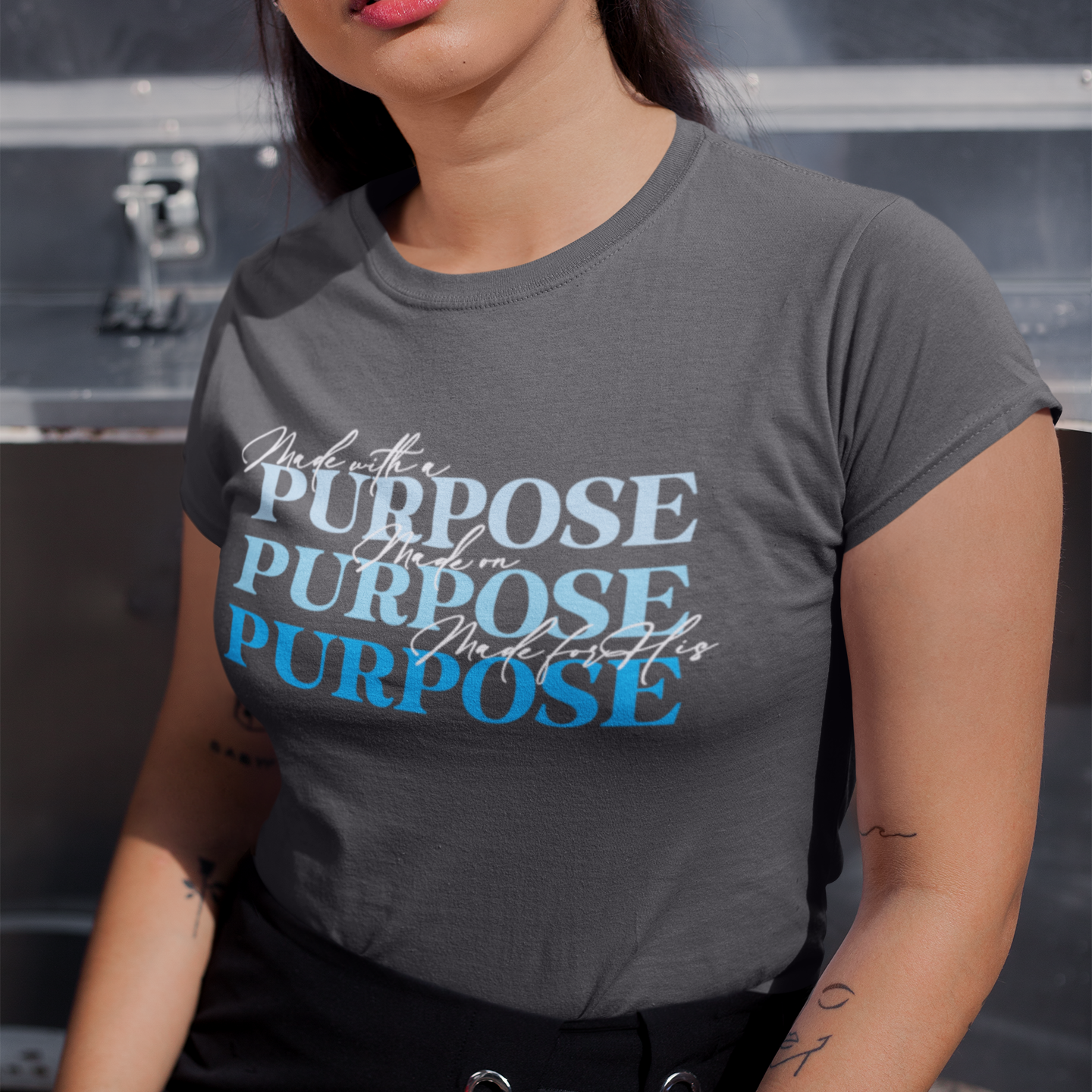 Woman wearing a gray t-shirt with motivational text, standing against a dark background.