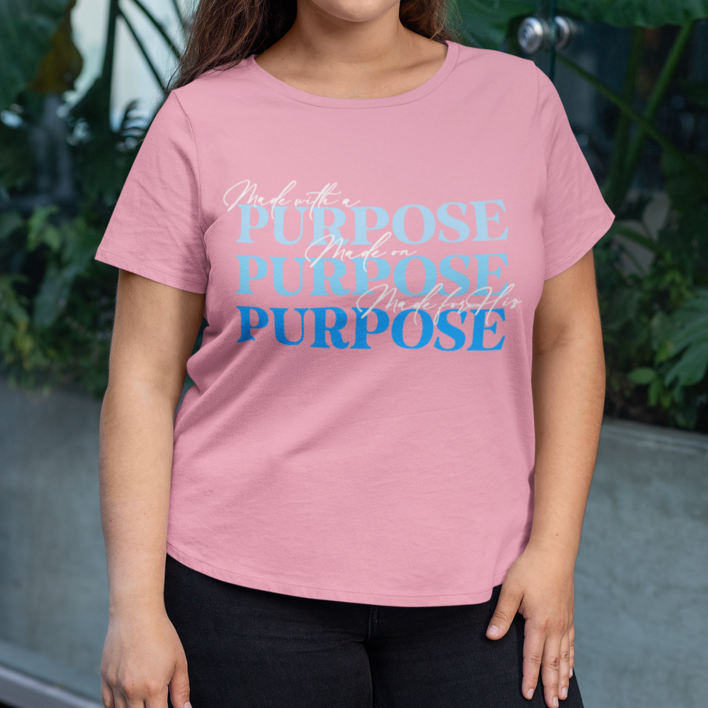 Person wearing a pink t-shirt with motivational text in front of green foliage