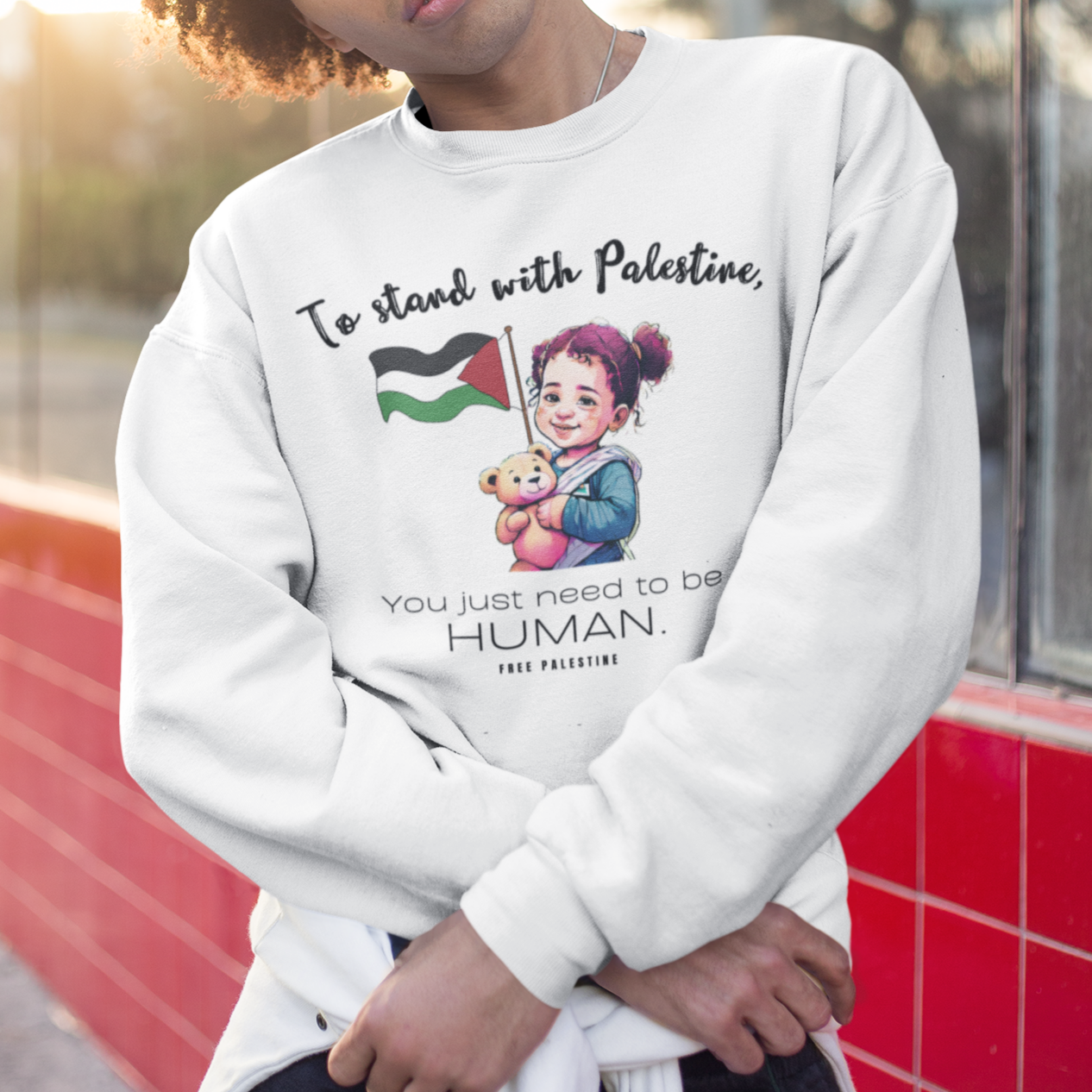 Person wearing a white sweatshirt with a message and graphic design, standing outdoors.