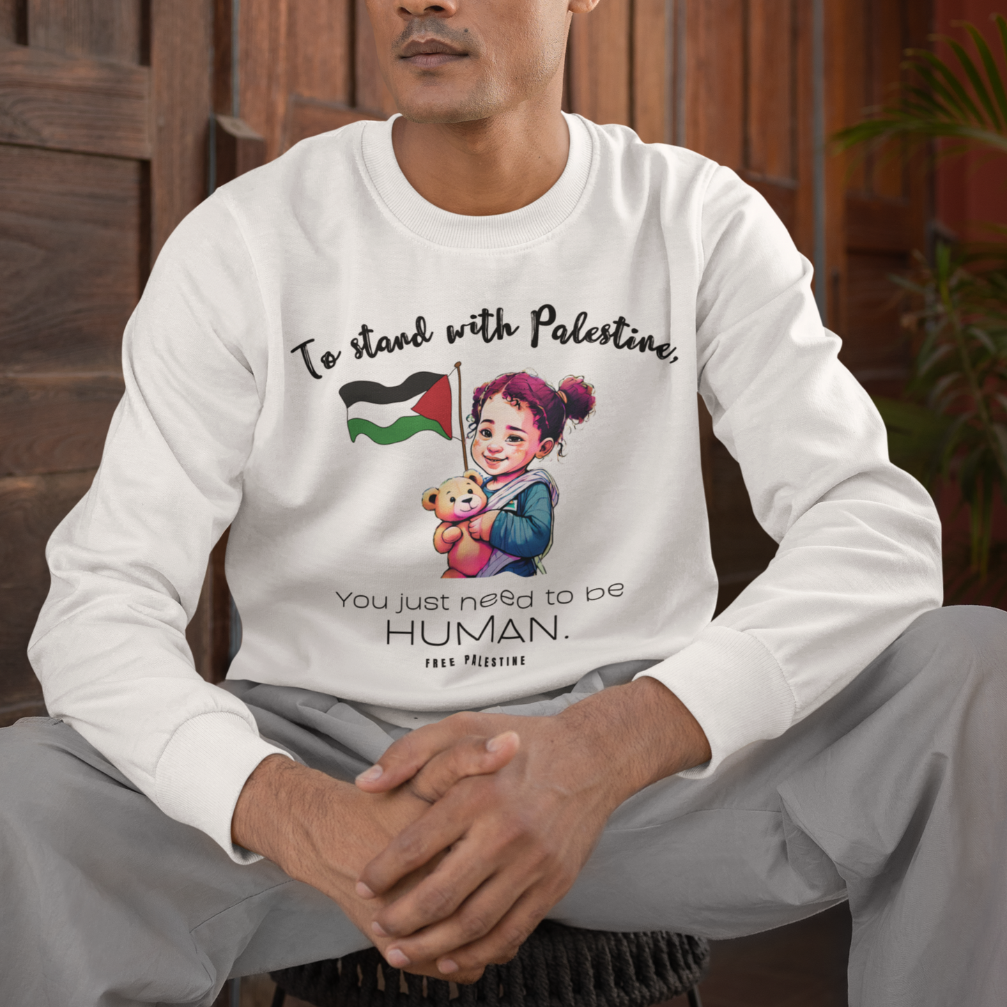 Person wearing a white long-sleeve shirt with a message and design, sitting indoors.