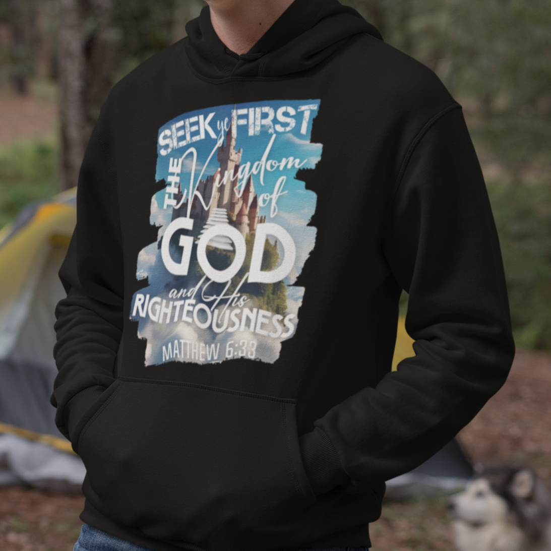 Person wearing a black hoodie with a graphic design outdoors, with a tent and dog in the background.