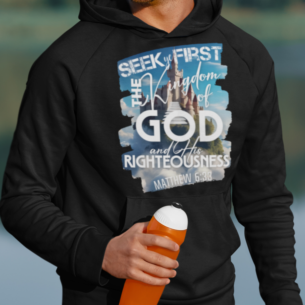 Man wearing a black hoodie with a motivational quote, holding an orange cup outdoors by a lake.