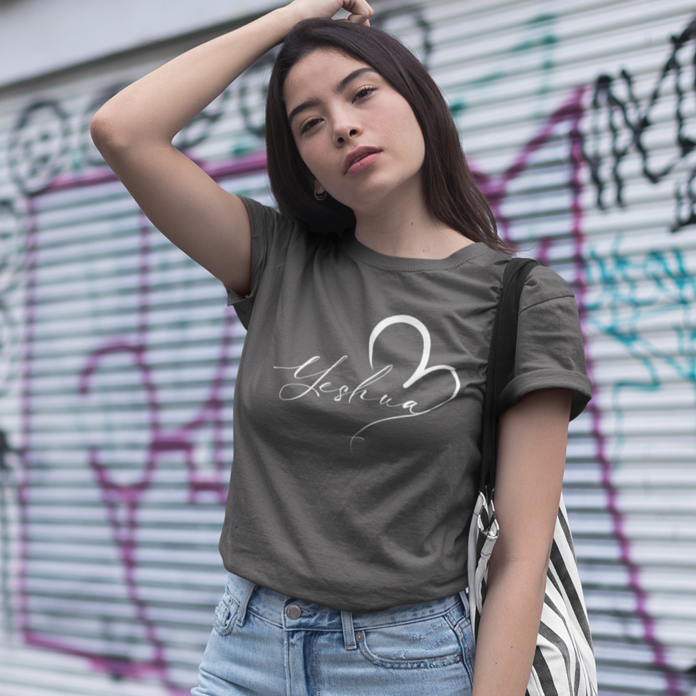 Woman wearing a gray t-shirt with a design and light blue jeans, standing in front of a graffiti-covered wall.